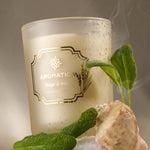 Aromatic candle with sage and mist label, surrounded by sage leaves and a shell on a textured surface.